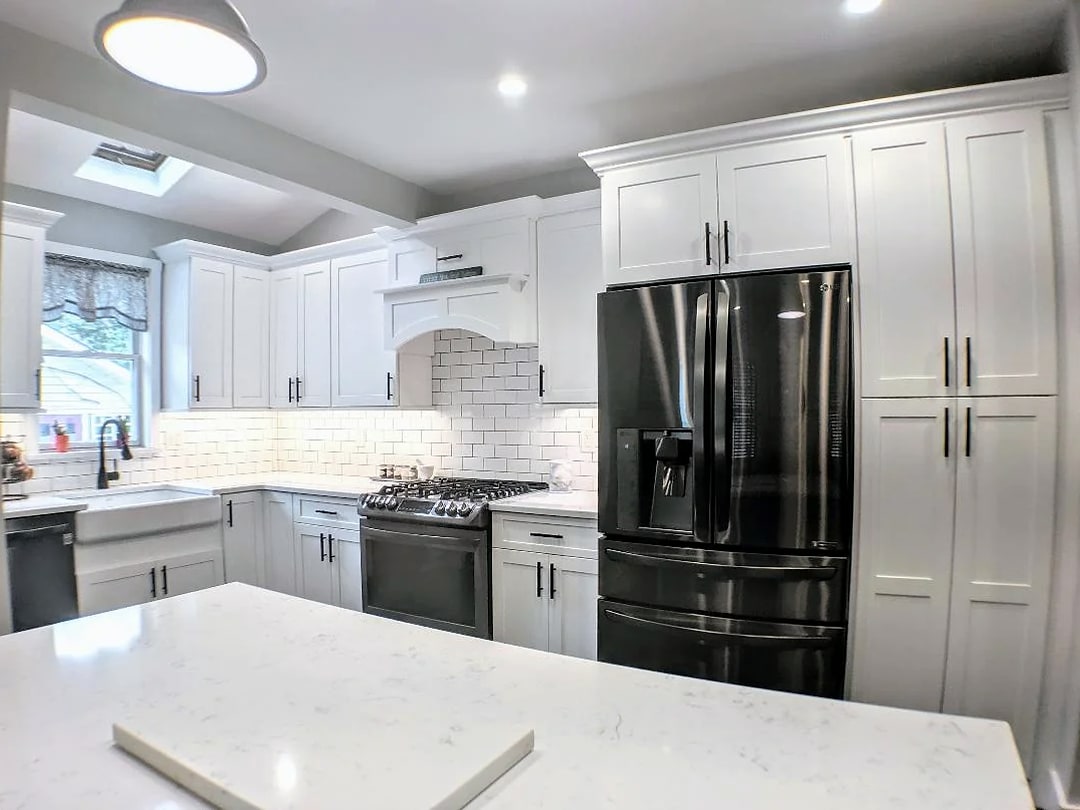White kitchen with black refrigerator, quartz island, skylight and farmhouse sink